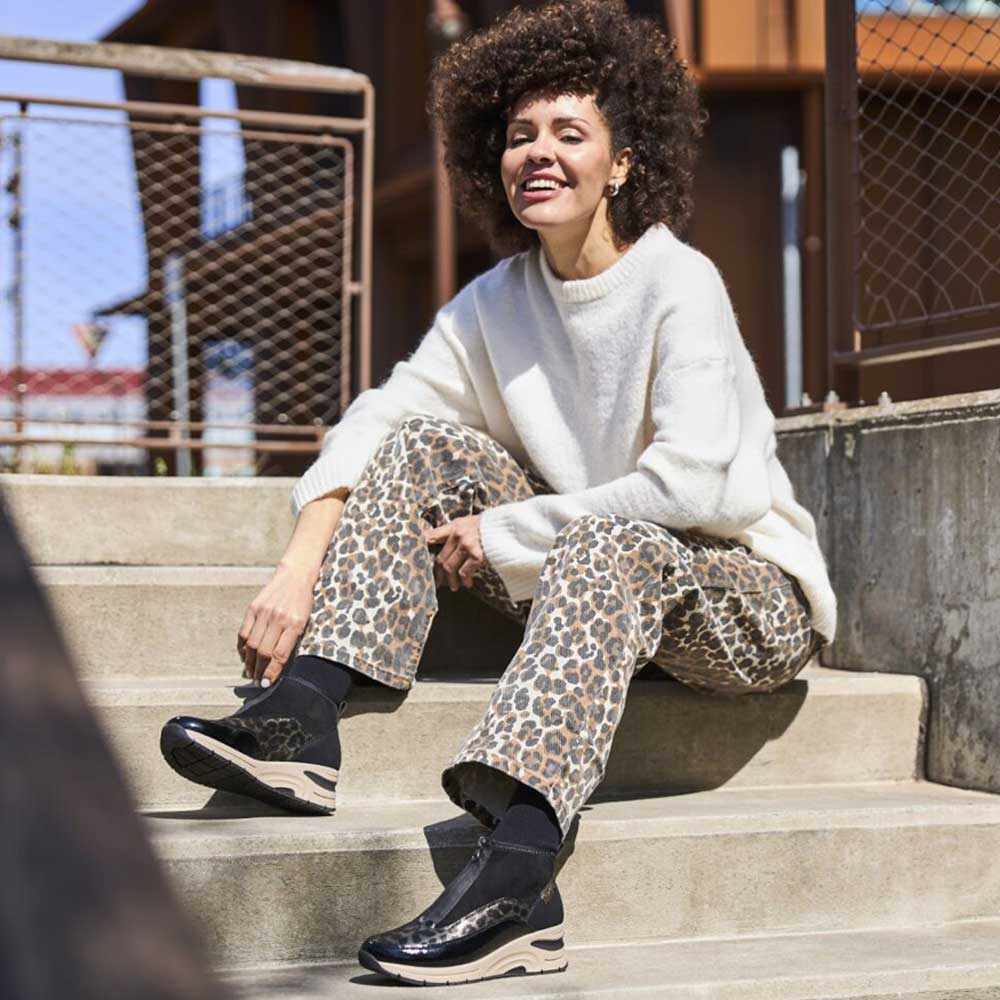 Woman sitting on steps wearing a white sweater, leopard print pants, and black boots.