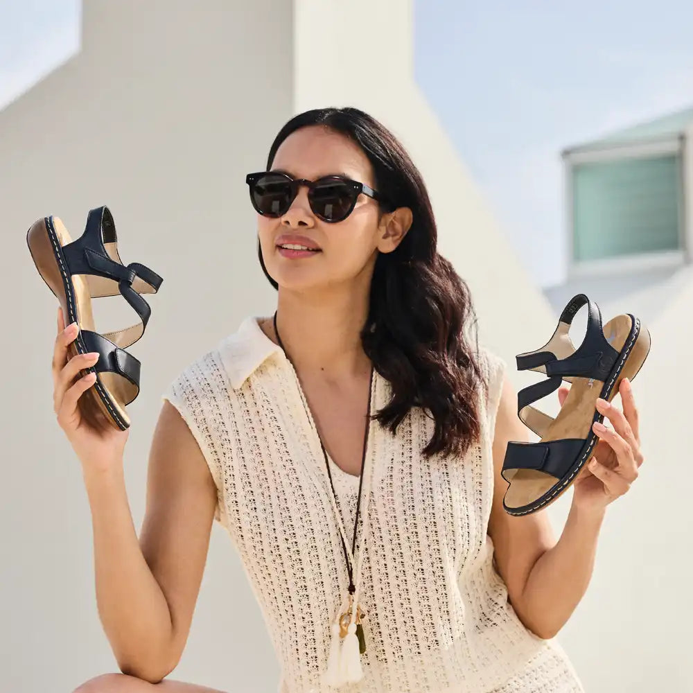 Woman holding two pairs of black sandals outdoors